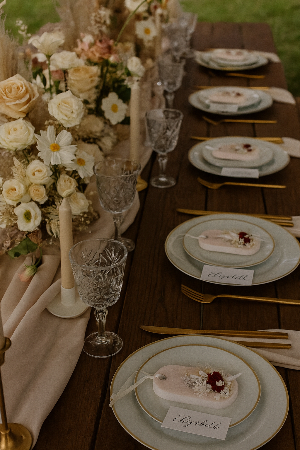 Elegant table setting with floral arrangement, guest favors, plates, and cutlery on a wooden table.