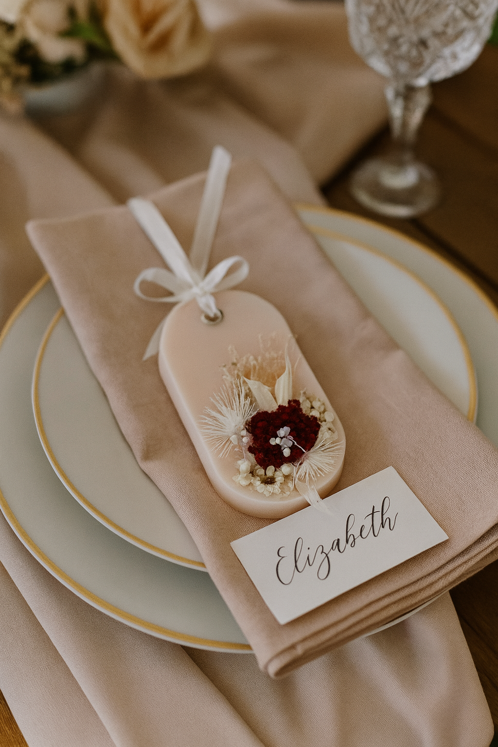 Decorative table setting with a name tag and small favor gift sachet on a beige napkin.