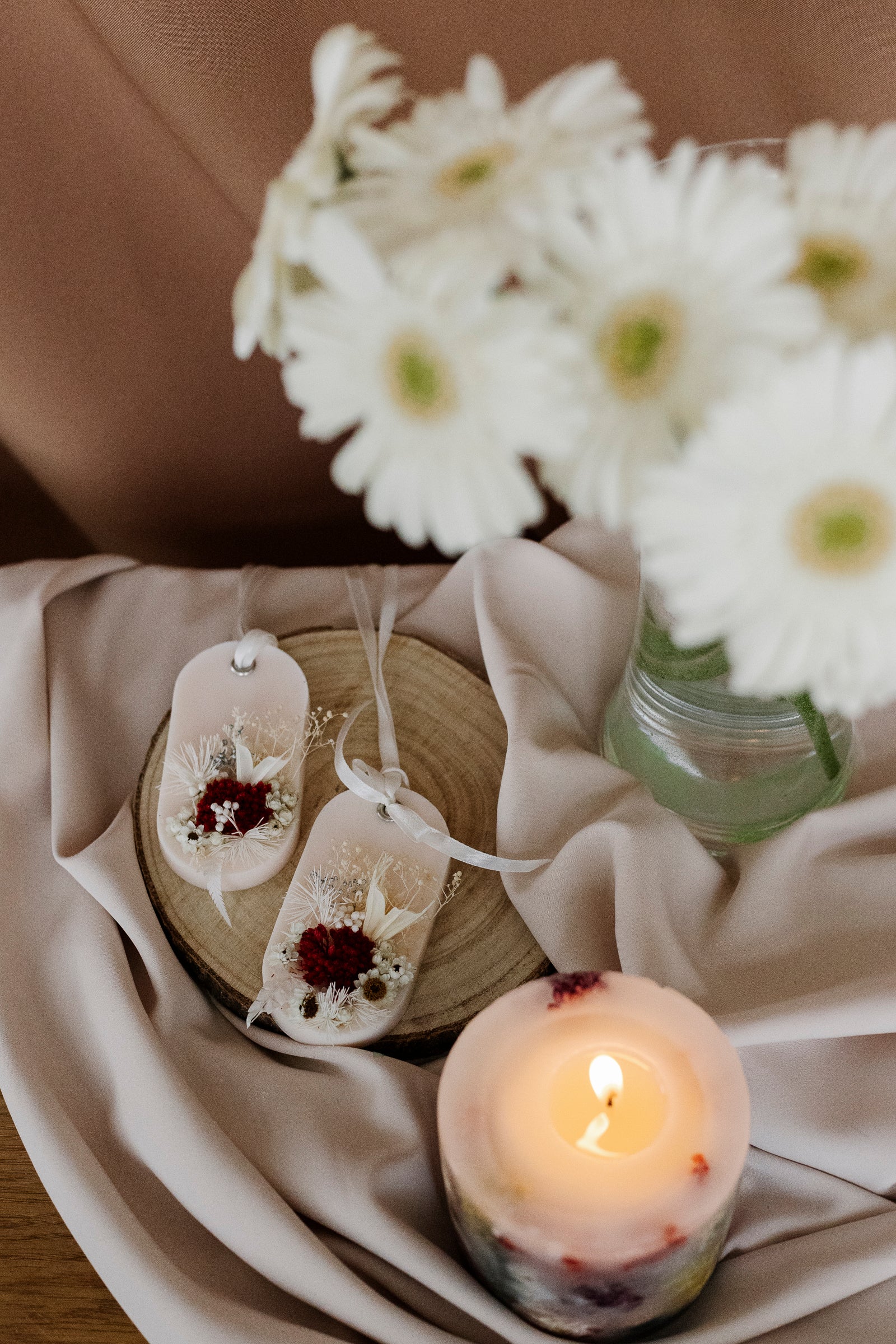 Candle with floral design and sachets in a vase on a soft fabric background