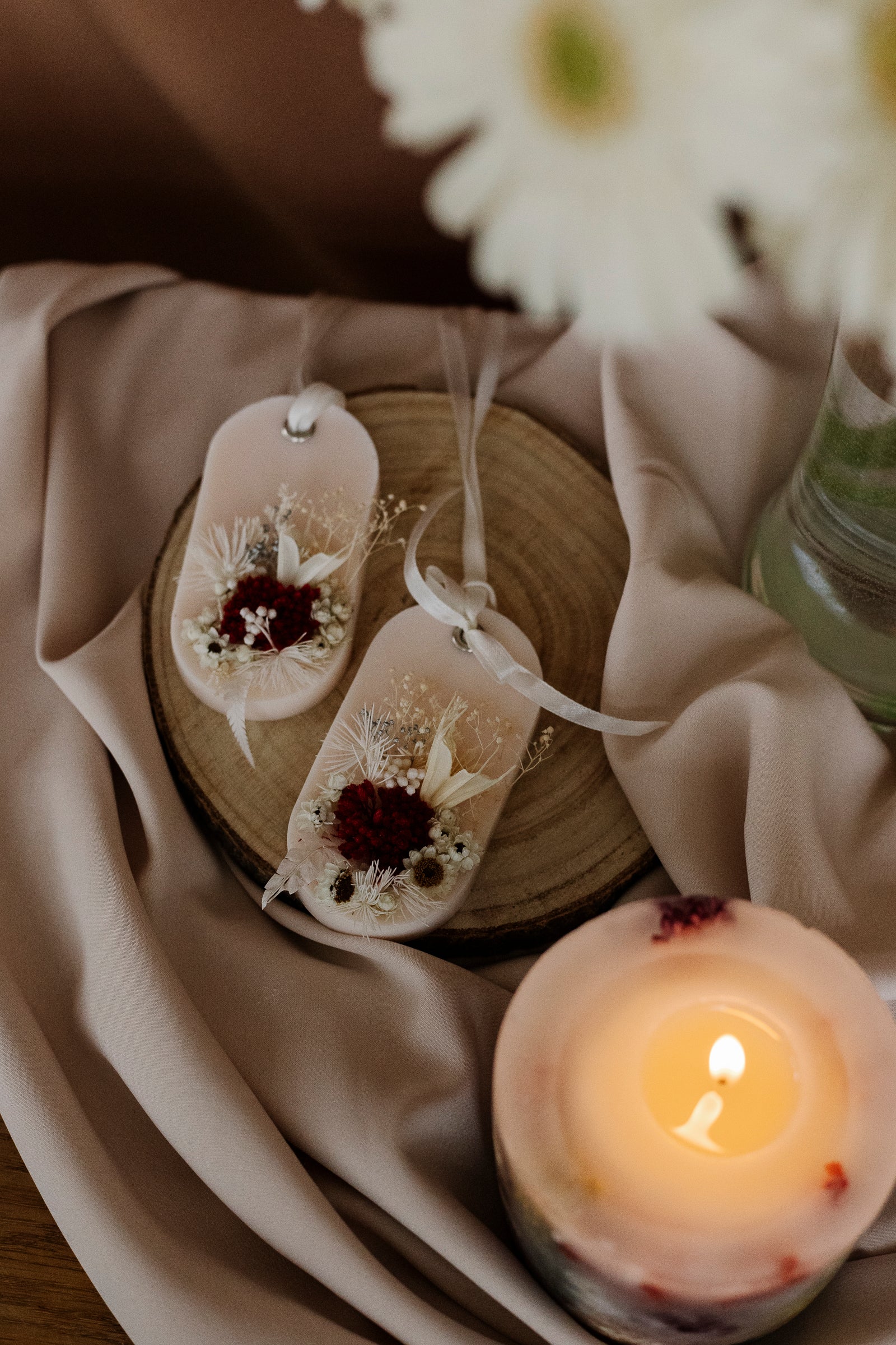 Decorative scented guest favors sachets with flowers on a wooden surface next to a lit candle.