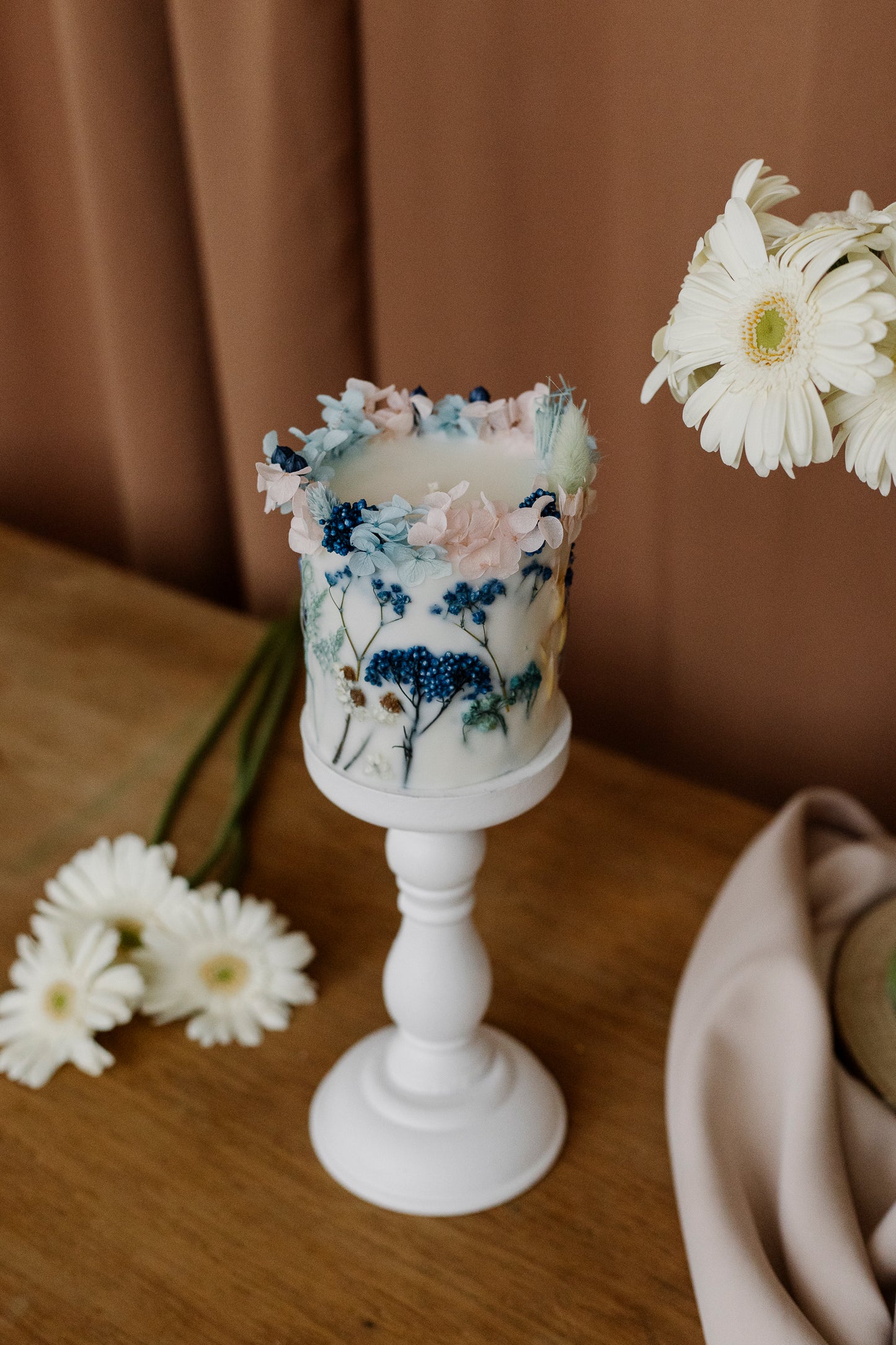 Decorative botanical candle with floral design on a wooden surface with flowers around