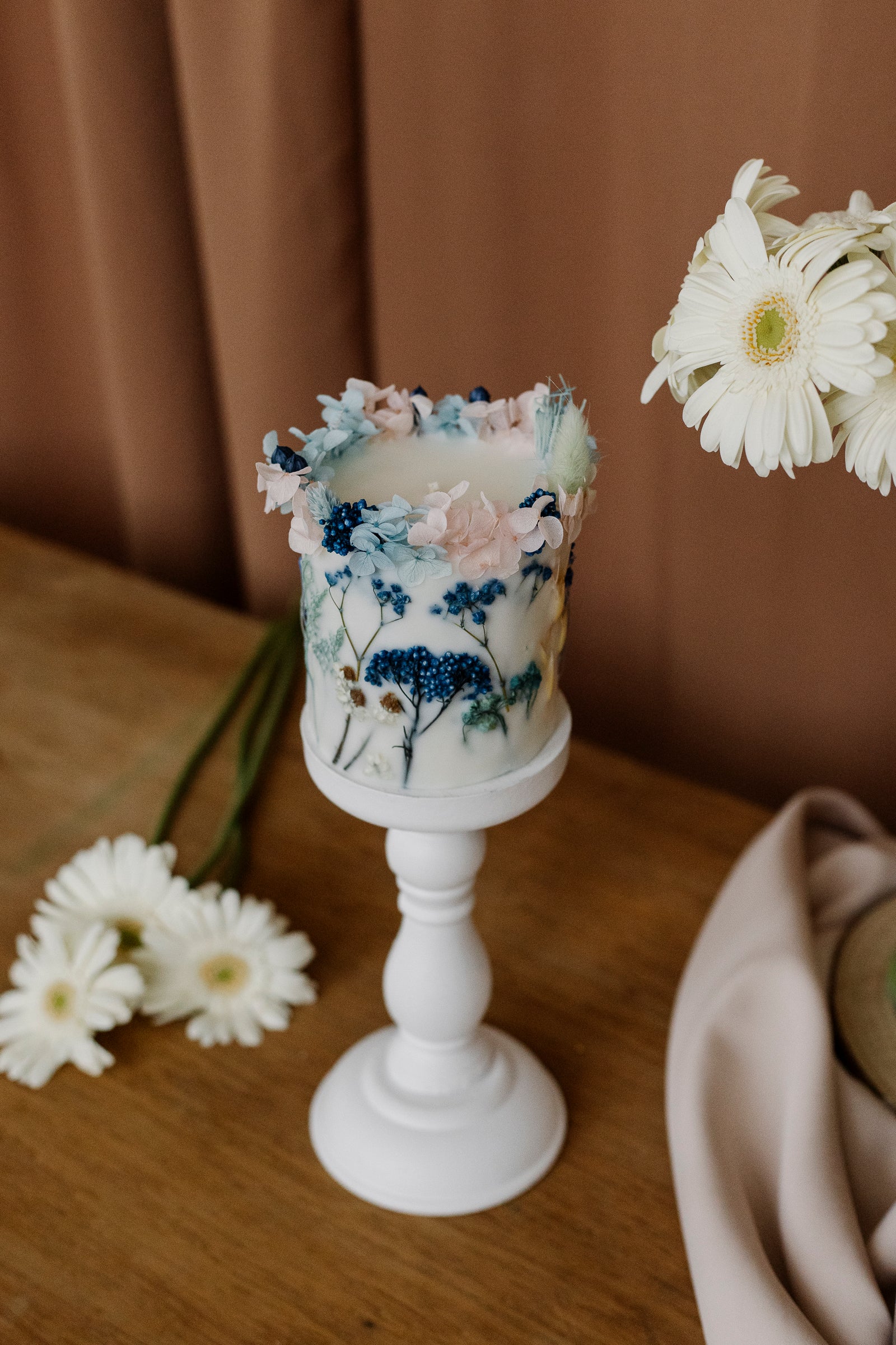 Decorative botanical candle with floral design on a wooden surface with flowers around