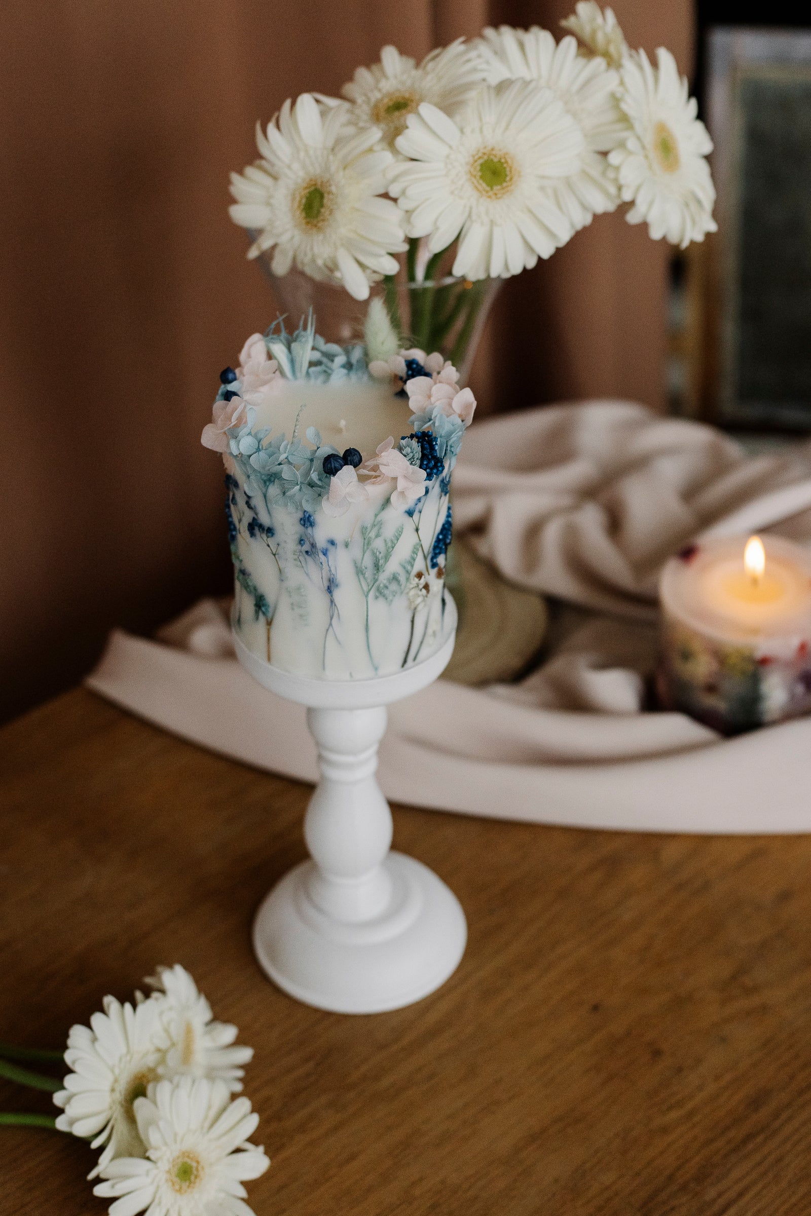 Decorative candle with floral design on a wooden surface, surrounded by white flowers.