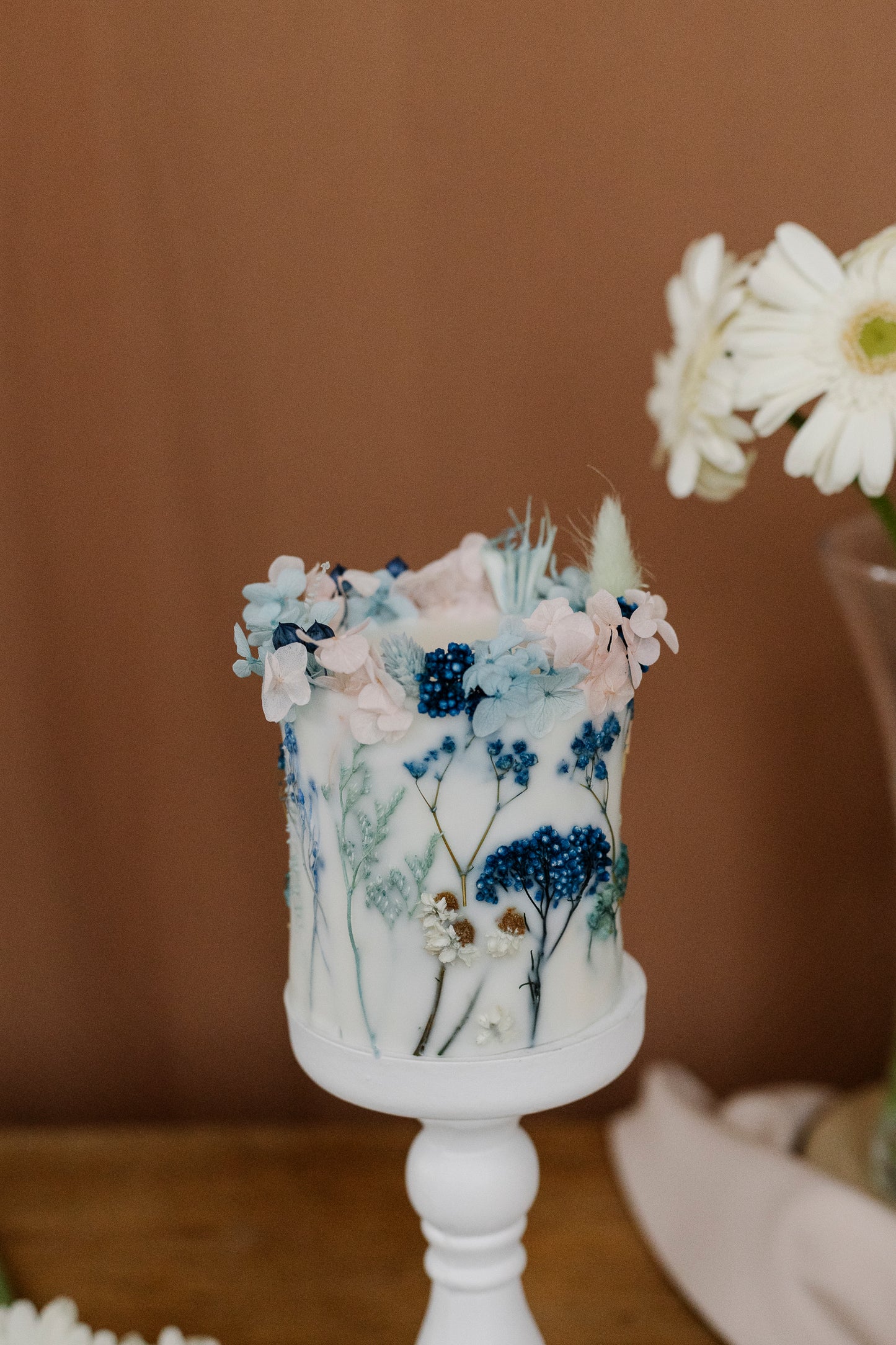 Botanical candle with floral decorations on a white stand against a brown background