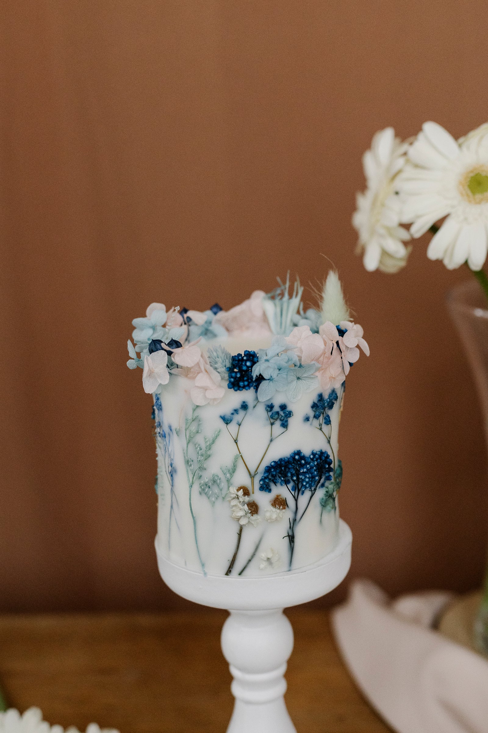 Botanical candle with floral decorations on a white stand against a brown background