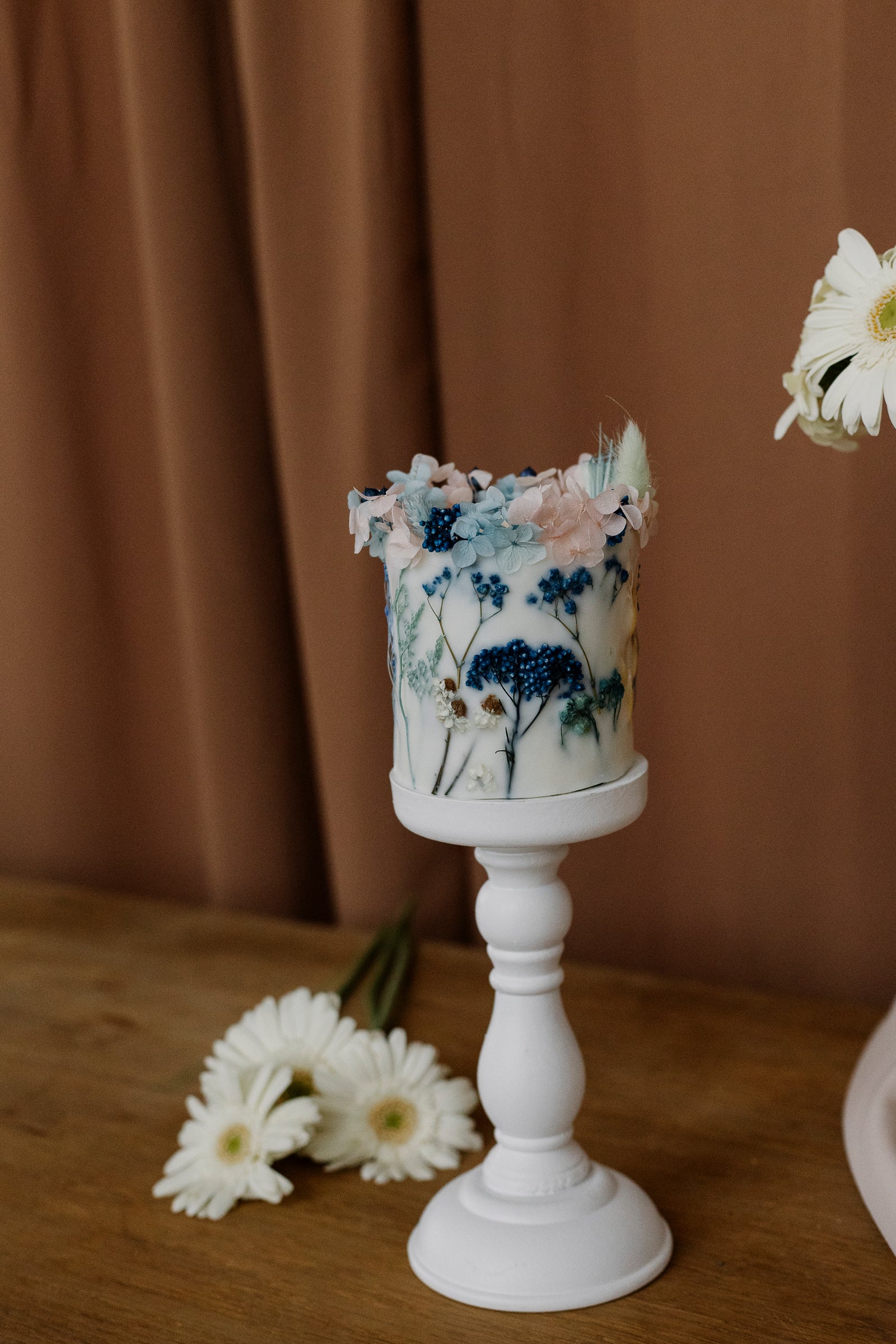 Decorative candle on a holder with floral design on a wooden surface and brown curtain background