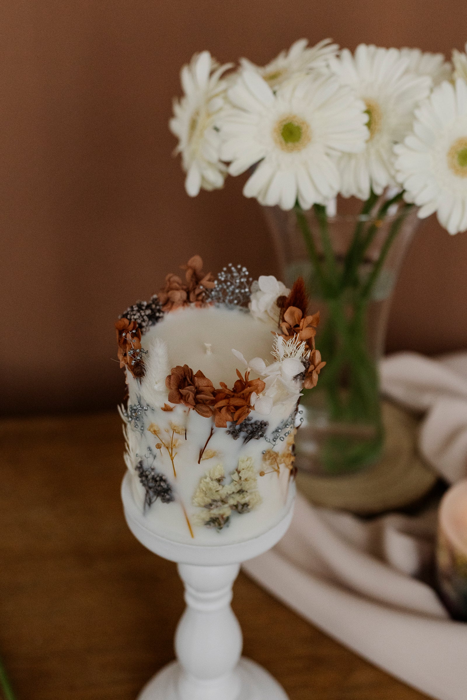 Decorative candle on a white stand with flowers in the background