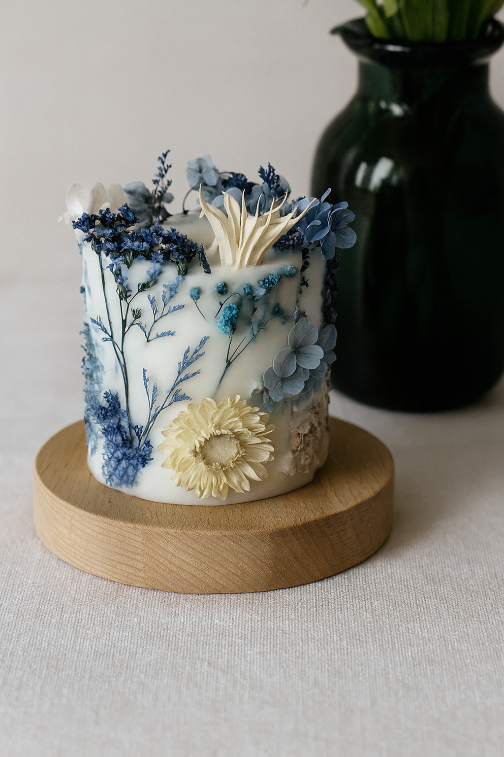 Decorative candle with floral design on a wooden base, with a dark vase in the background.