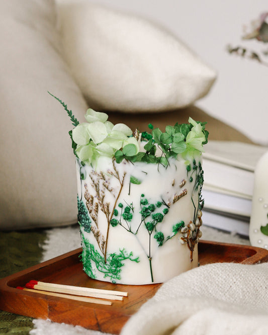 Decorative candle with floral design on a wooden tray in a cozy living room setting.