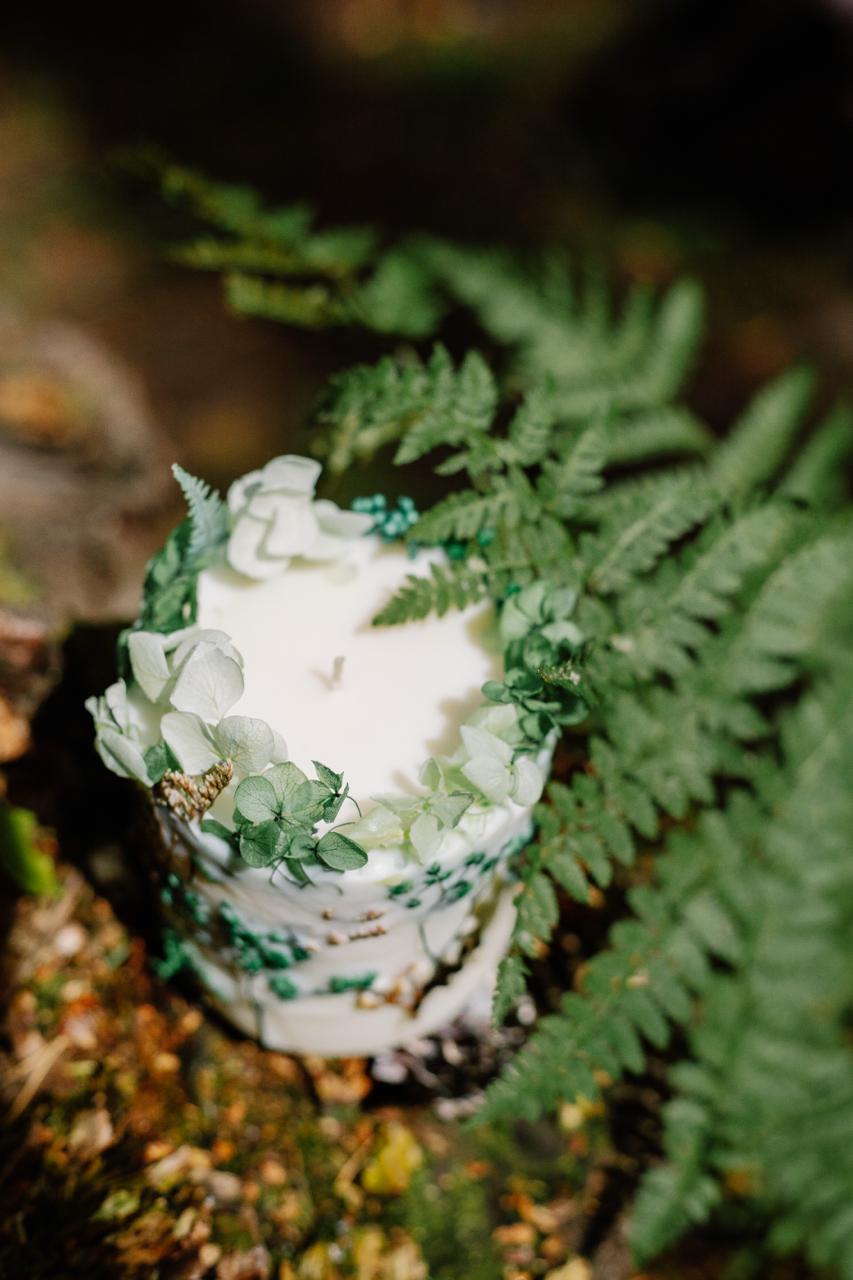 Small white botanical candle with green decorations on a bed of ferns