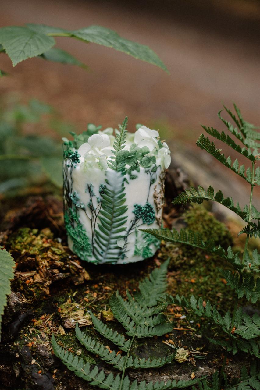 Decorative candle with nature-themed design on a bed of ferns and moss
