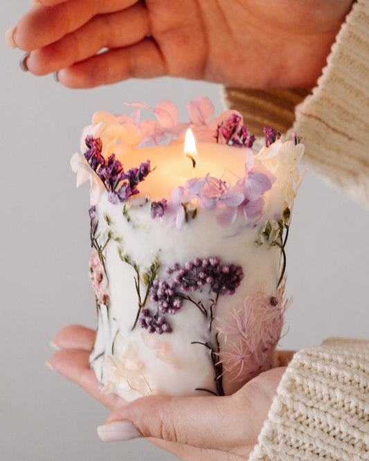 Hand holding botanical candle with floral design against a neutral background