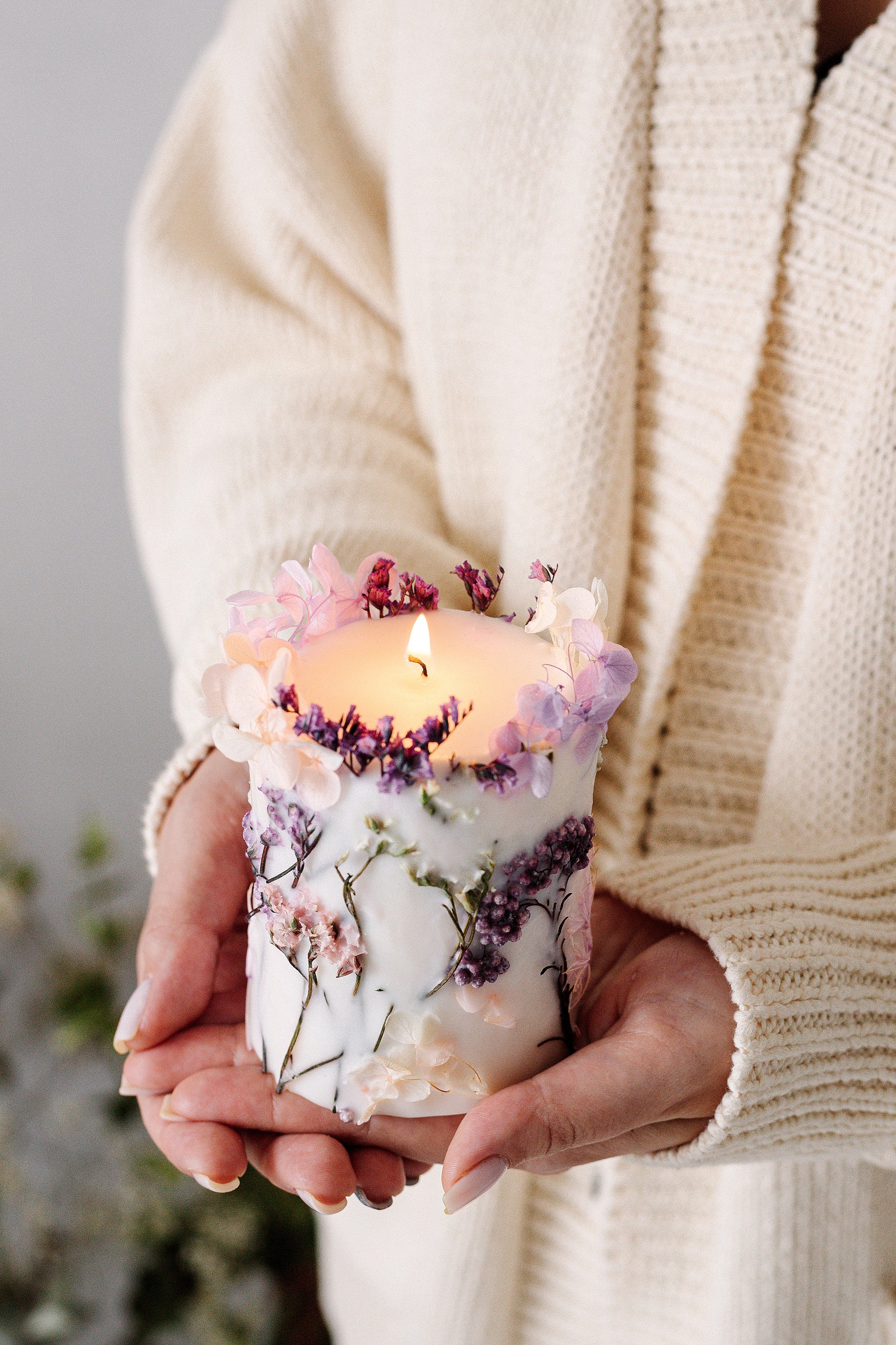 Person holding a botanical candle with floral design in a cozy setting