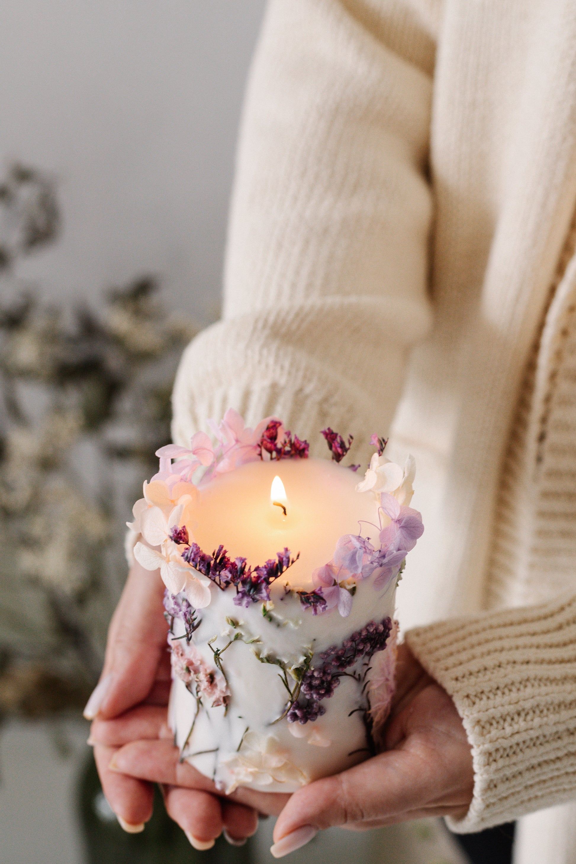 Person holding a candle with floral decorations in a blurred indoor setting