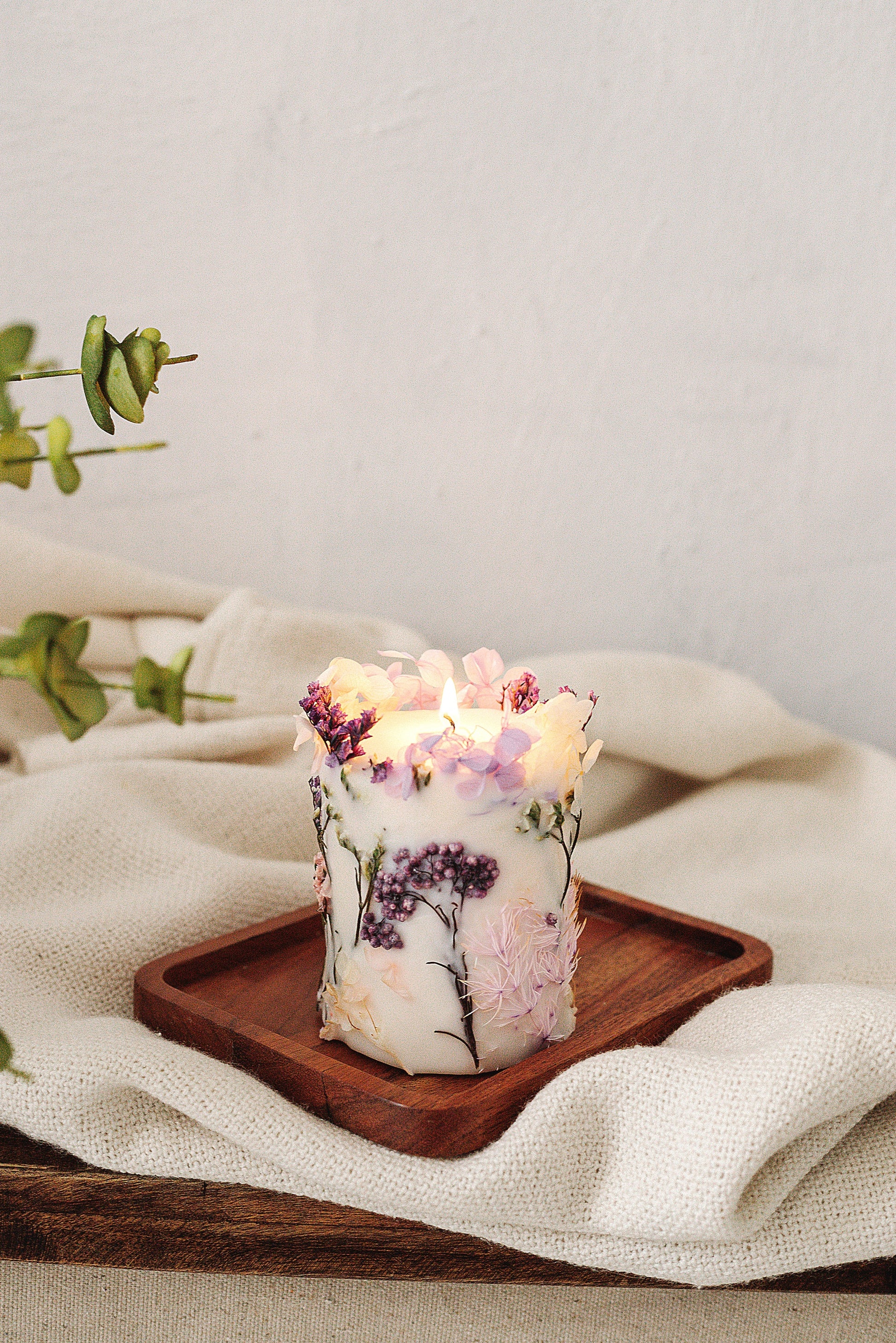 Decorative candle with floral design on a wooden tray on a light fabric background