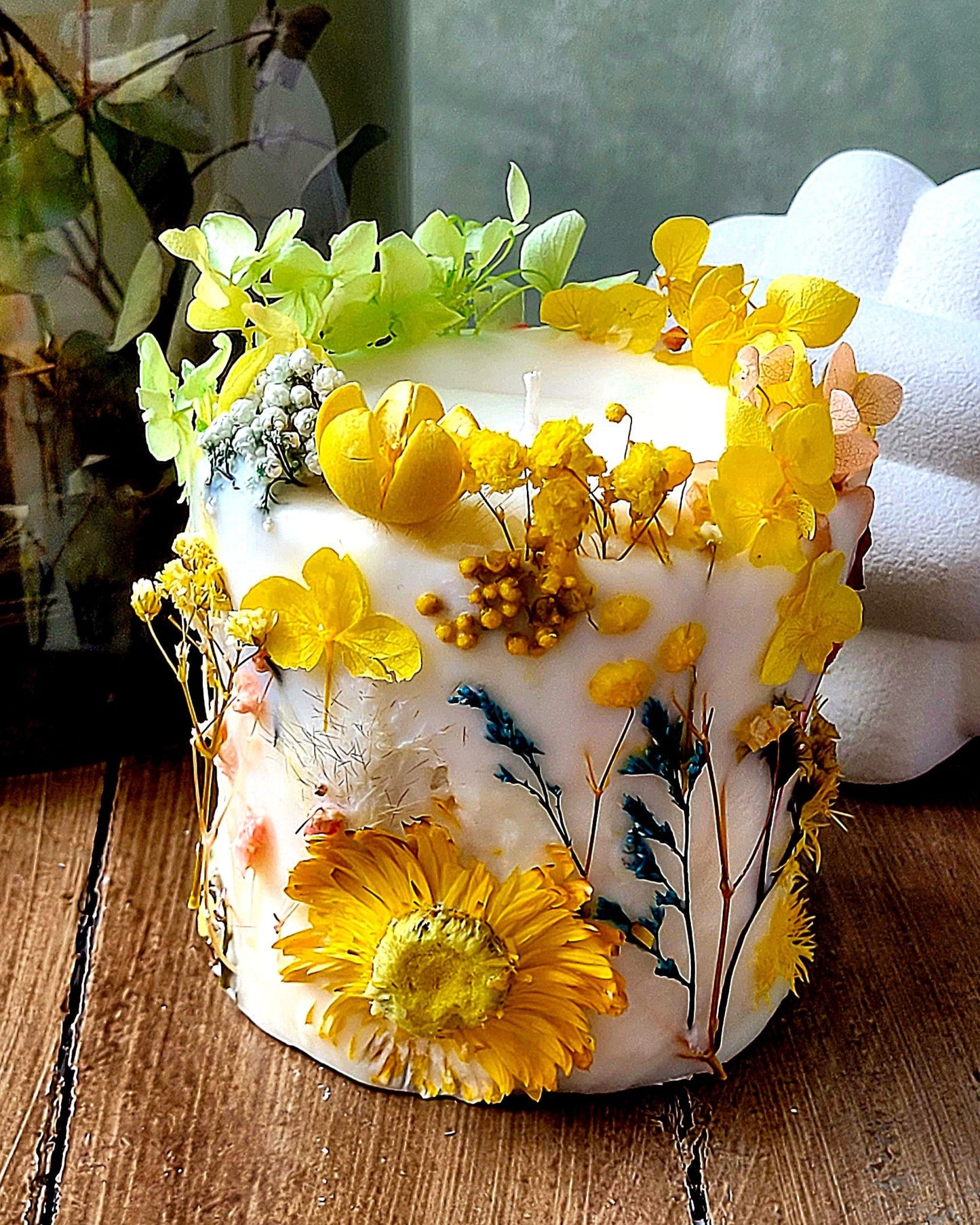 Decorative botanical candle with yellow flowers on a wooden surface