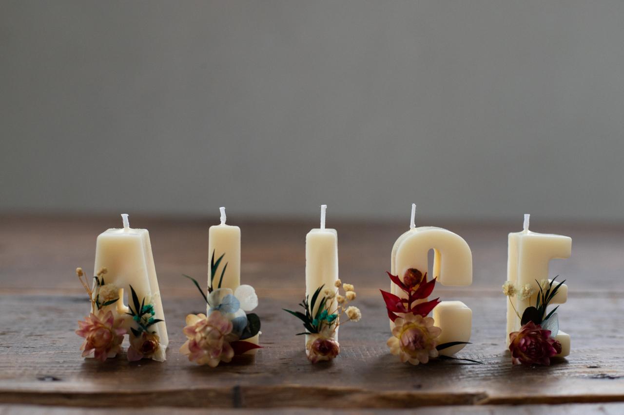 Candle letters spelling 'Alice' with floral decorations on a wooden surface.