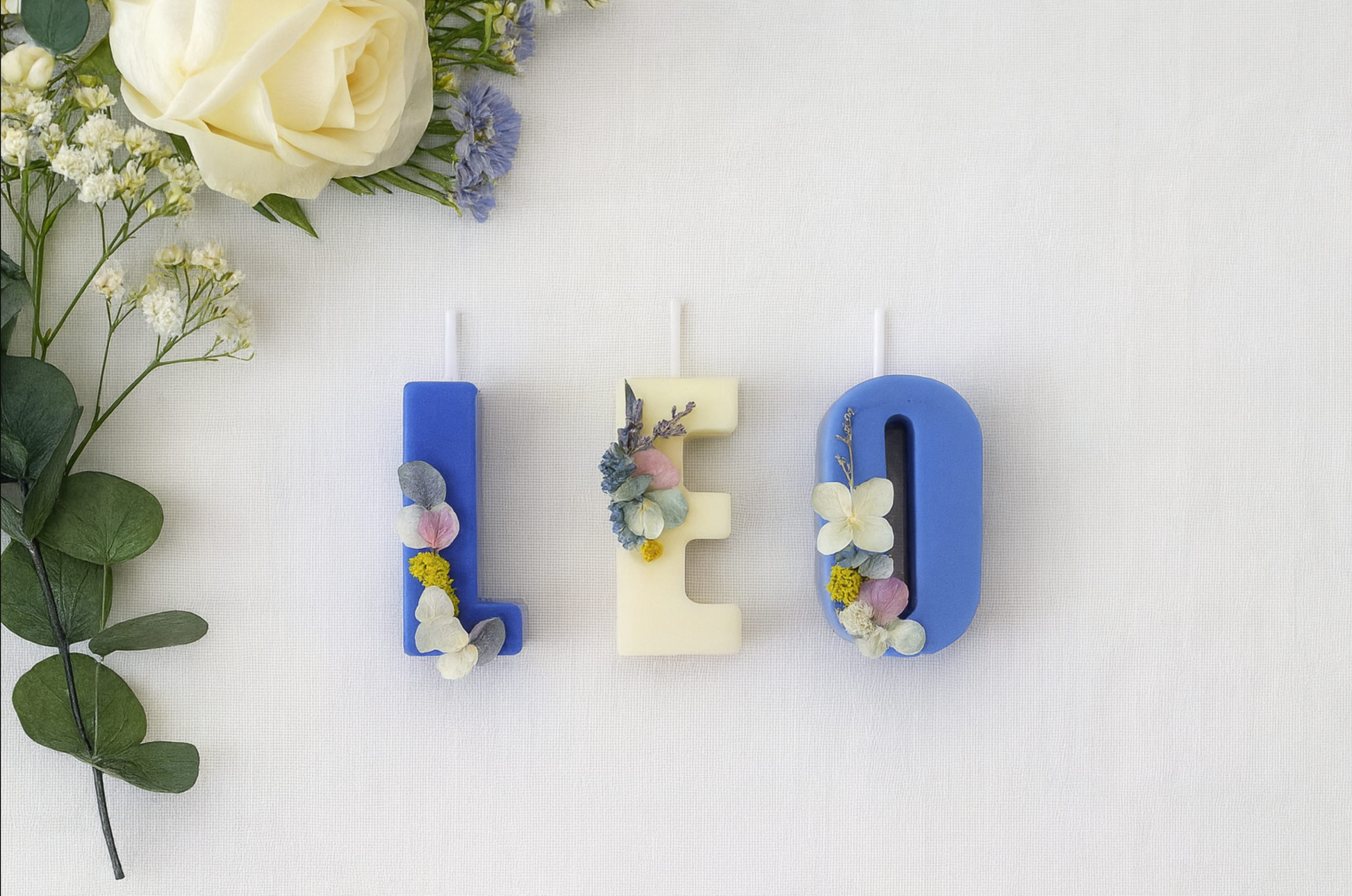 Decorative letter candles 'L', 'E', 'O' with floral elements on a white background