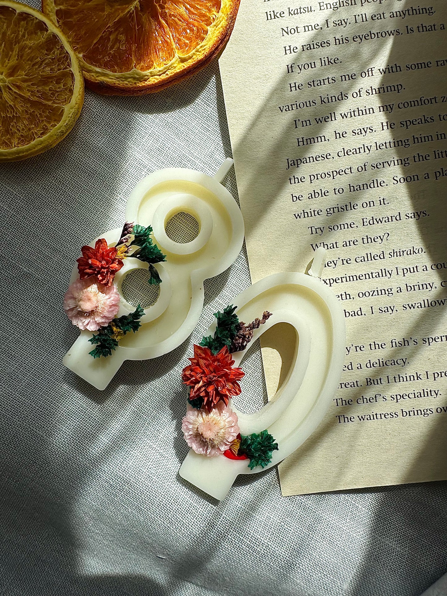 Decorative number candles with flowers on a textured surface next to dried oranges and an open book.