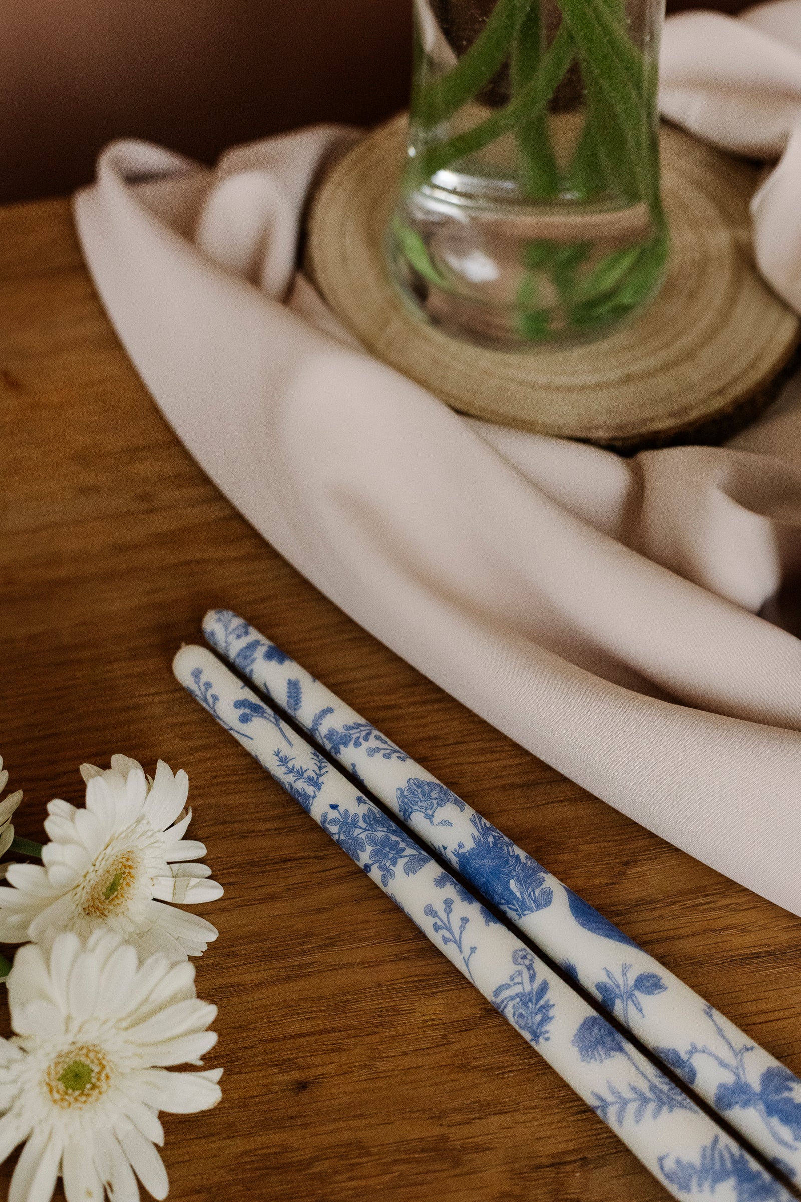 Two blue and white patterned candles on a wooden surface with a ceramic hand and white flowers in the background.
