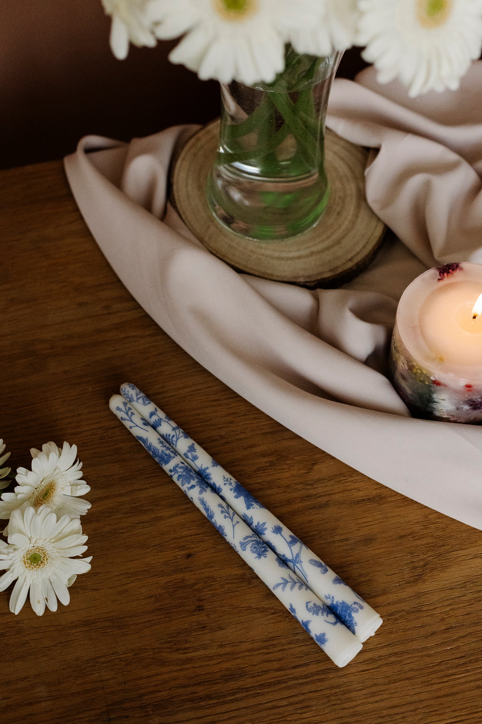 Two blue and white patterned candles on a wooden surface with white flowers and a candle in the background.