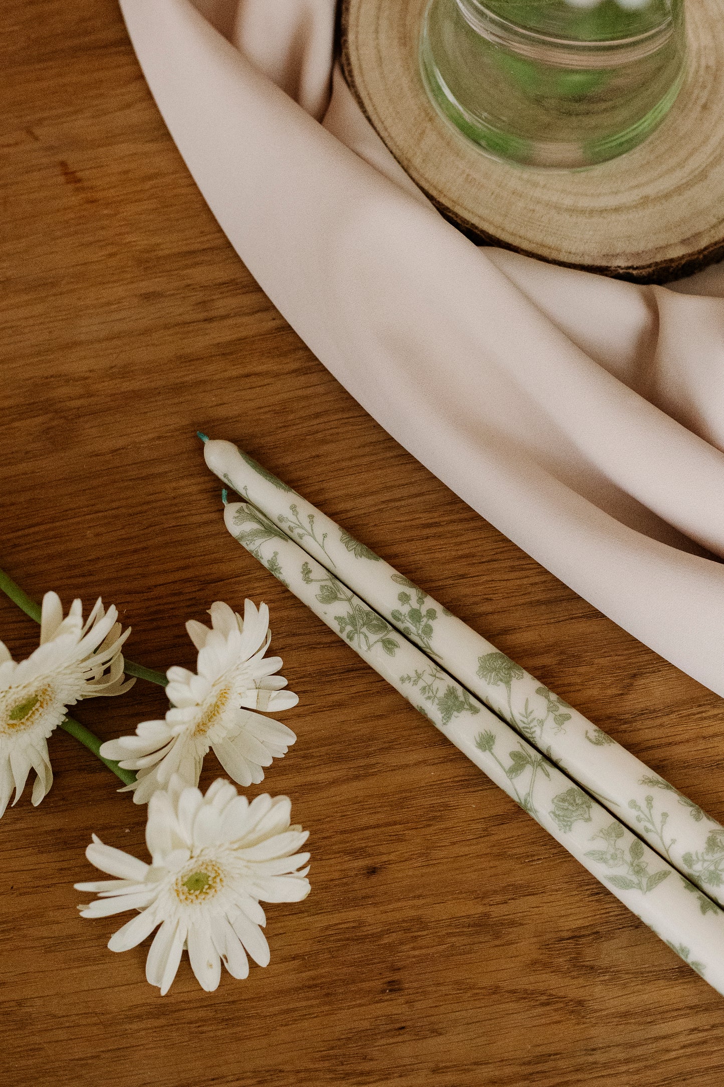 White flowers and patterned candles on a wooden surface with a white cloth.