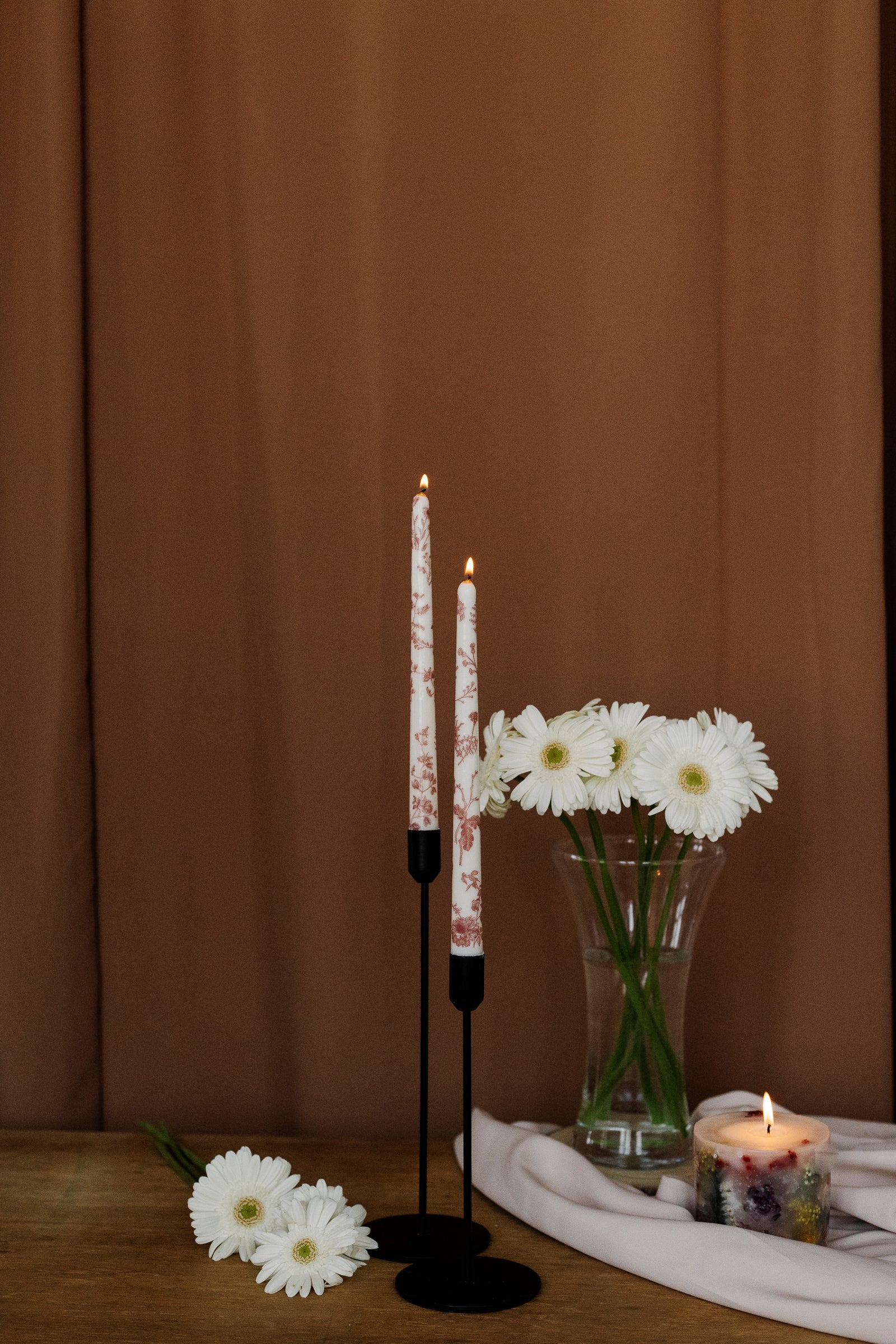 Decorative setup with candles, flowers, and a candle on a wooden surface against a brown background