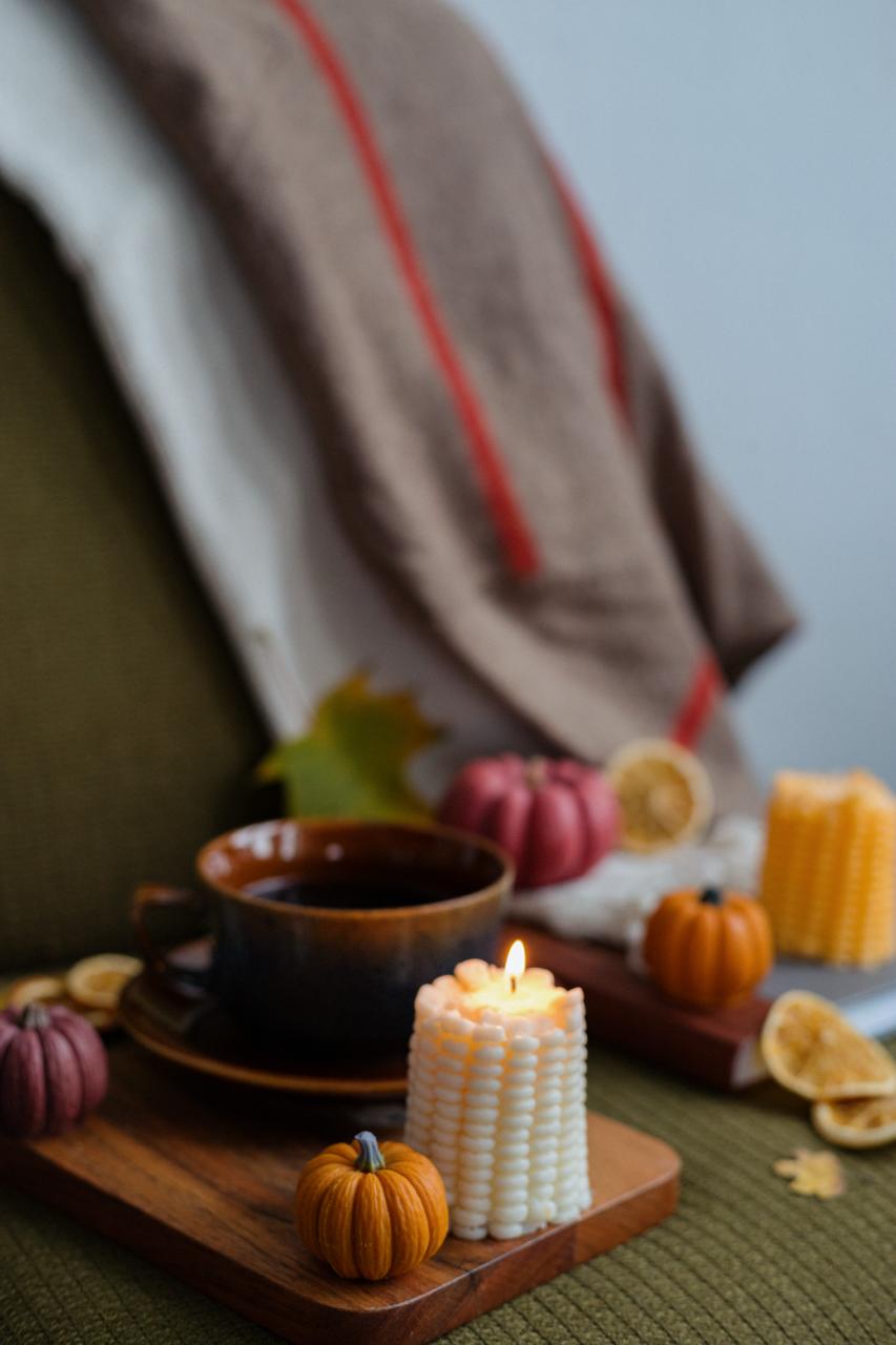 Candle, mug, and pumpkins on a wooden board with a blanket in the background