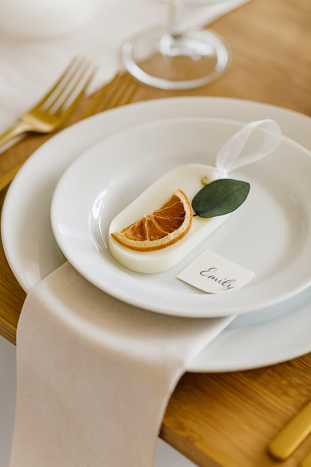 Table setting with a party favor on a white plate, lemon wedge, and leaf on a wooden table.