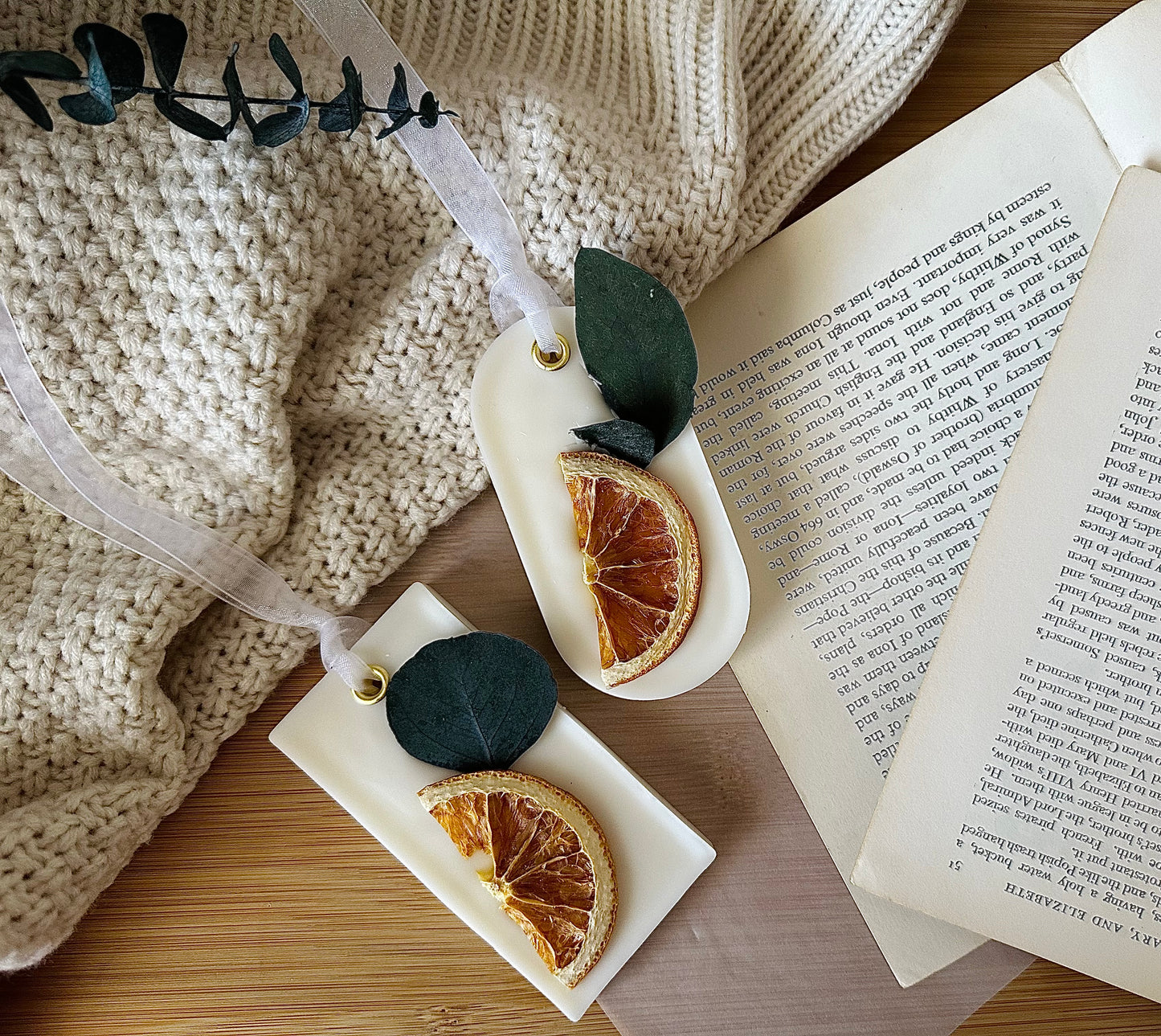Decorative sachet with dried oranges and leaves on a marble tray next to an open book.