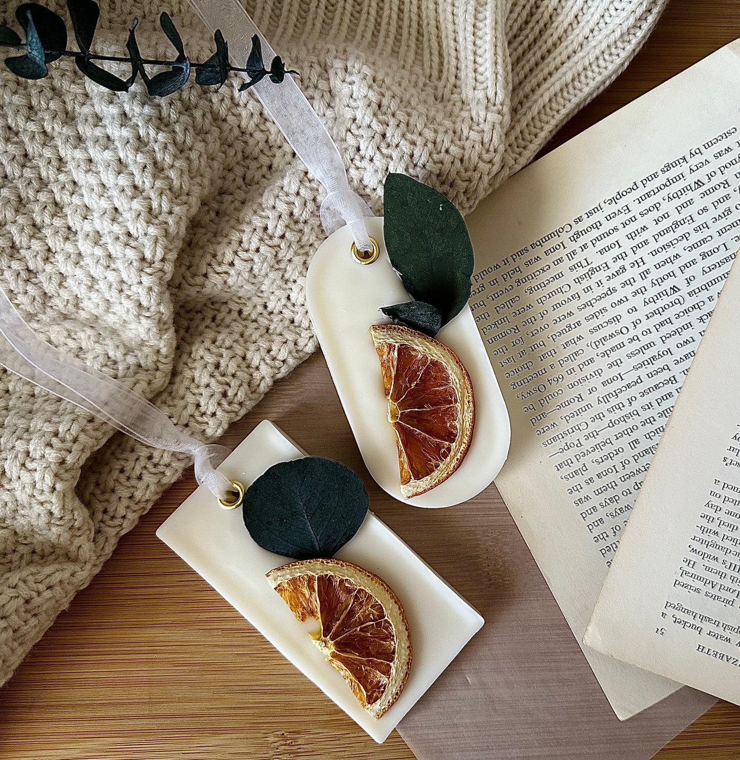 Decorative sachet with dried orange slices and leaves on a wooden surface next to an open book.