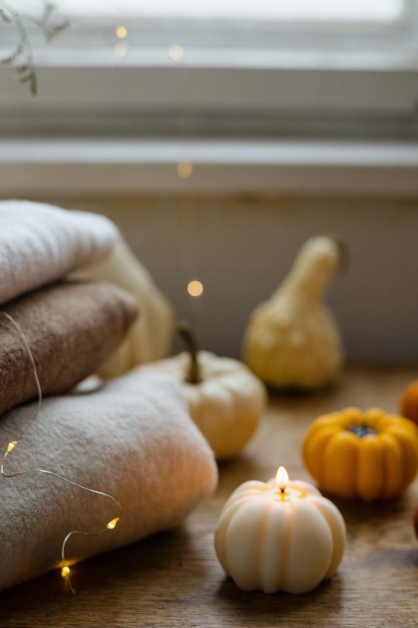 Small pumpkin candle on a wooden surface with pumpkins and string lights in the background.