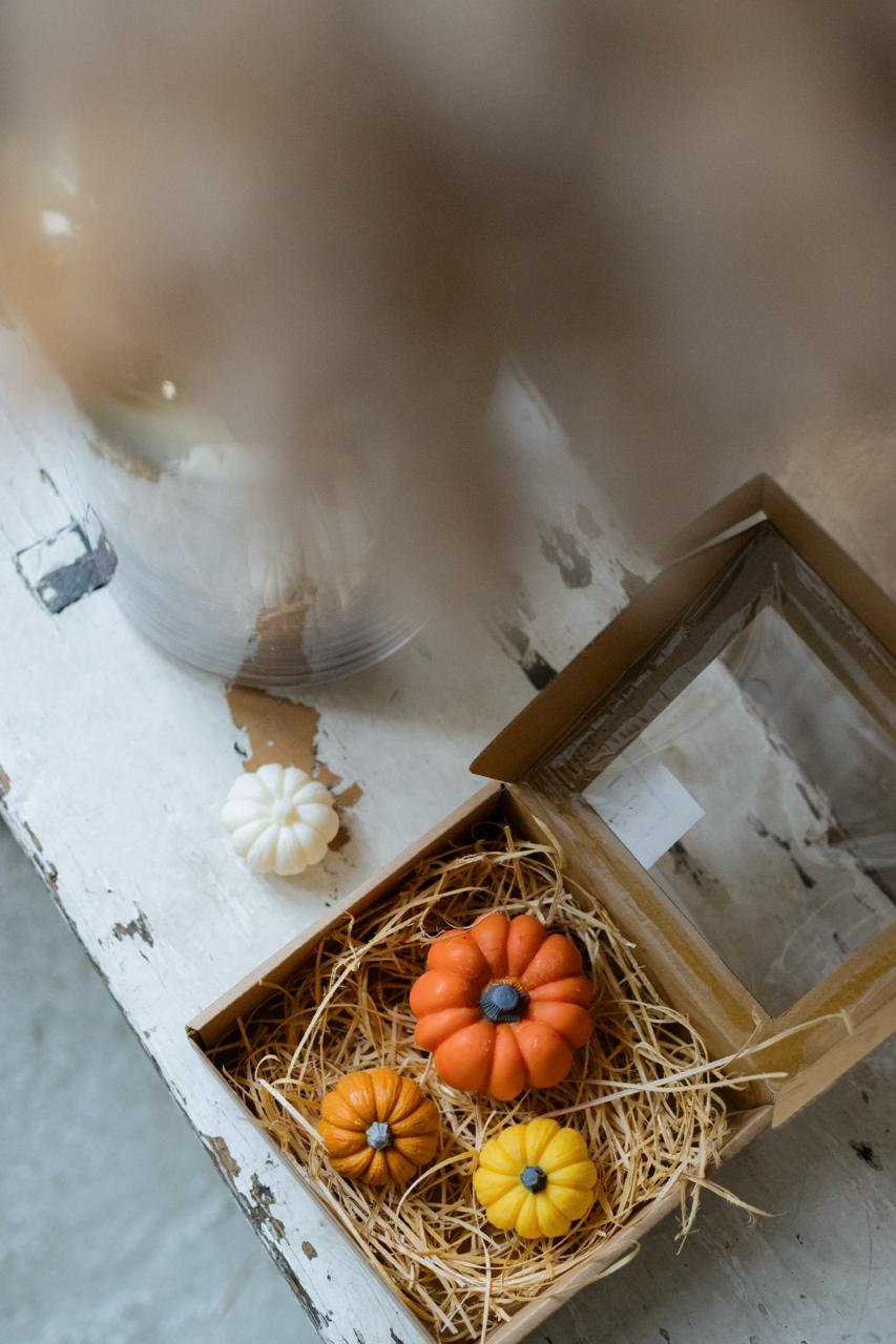 Decorative pumpkin candles in a box with straw on a rustic wooden surface